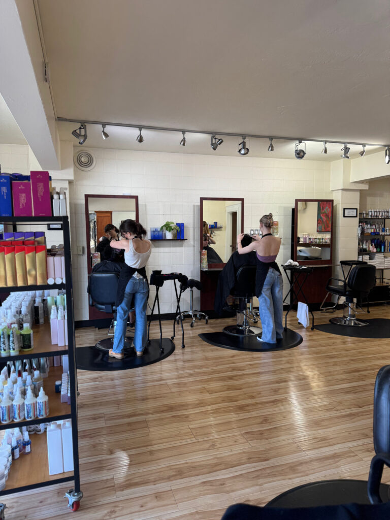 Stylists at work at their stations on the willow hair salon floor, with retail products on the shelf at left